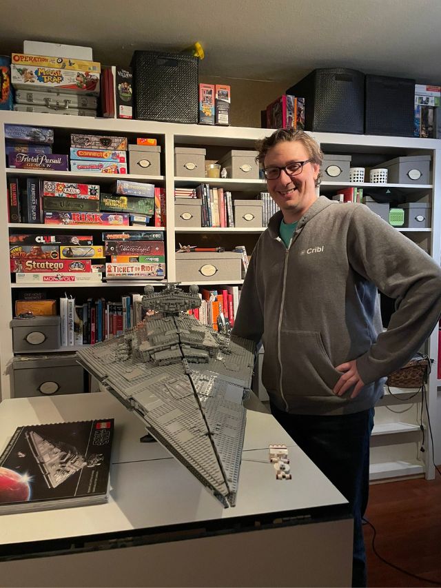 Cribl Founder Clint Sharp Net Worth, Career Journey, Vision & Growth 2
Clint Sharp, the founder of Cribl, stands proudly next to a massive LEGO Star Destroyer in a room filled with books and games.