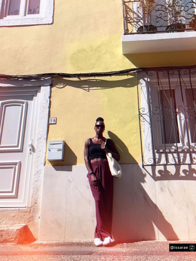 HOORAE Media Founder Issa Rae Net Worth, Hollywood Success Story, Vision & Brand Growth 2
Issa Rae, founder of HOORAE Media, poses stylishly against a yellow wall wearing dark sunglasses and a chic, casual summer look.