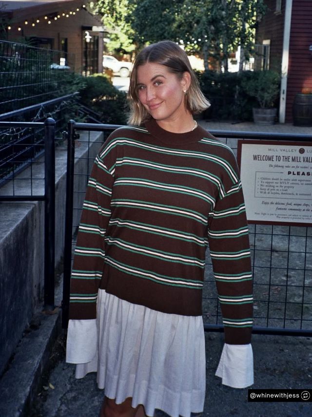 Jess Druey Net Worth, Whiny Baby Wine Founder Journey Vision and Market Growth 2 Jess Druey, founder of Whiny Baby Wine, poses outdoors wearing a brown striped sweater and a white pleated skirt.