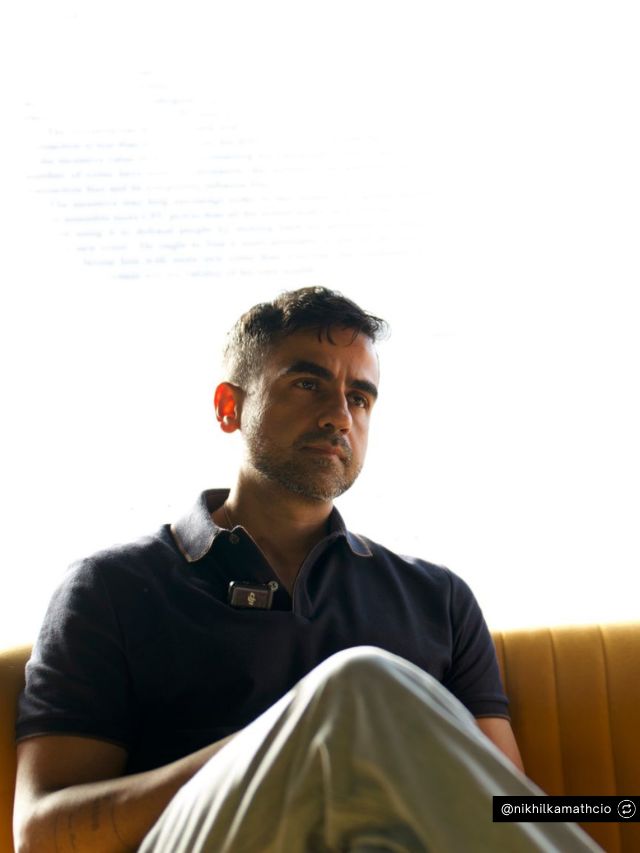 Zerodha Co-Founder Nikhil Kamath Net Worth, Entrepreneur Journey & Success 2 Nikhil Kamath, co-founder of Zerodha, sits thoughtfully on a yellow sofa while wearing a casual navy polo shirt in soft light.