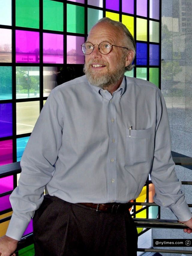 Adobe Co-Founder John Warnock Net Worth, Entrepreneur Journey & Success 2 John Warnock, the co-founder of Adobe, smiles warmly while posing in a light blue shirt before a vibrant, colorful glass wall.