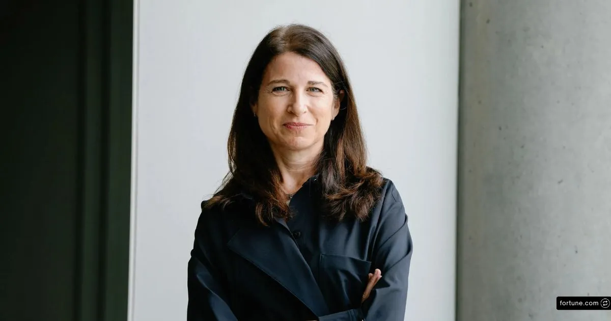 Daydream Founder Julie Bornstein Net Worth and AI Business Journey 4 Julie Bornstein smiles confidently, wearing a dark navy button-up coat while posing against a bright, minimalist white wall.