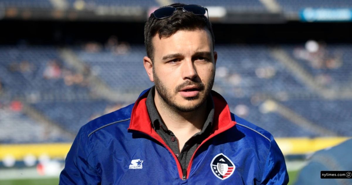 Infinite Athlete Founder Charlie Ebersol Net Worth, Sports Tech Vision & Growth 4 Charlie Ebersol stands in a stadium, wearing sunglasses and an official blue sports jacket.